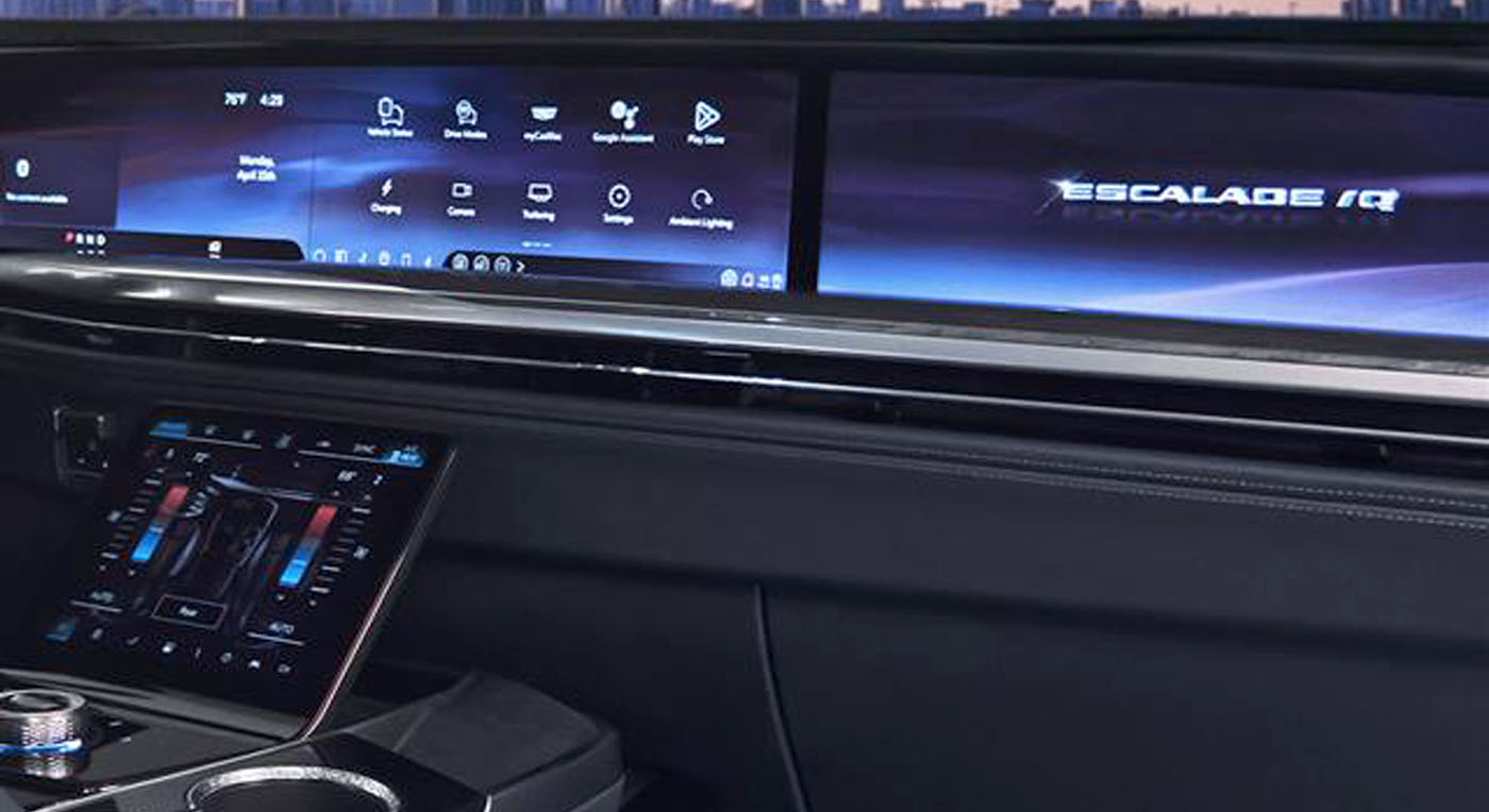 The image shows the sleek interior of a Cadillac Escalade IQ, featuring a wide digital dashboard with touchscreen controls and a modern, tech-savvy ambiance.